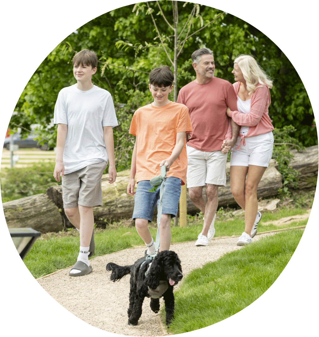 Family enjoying a relaxing walk with their dog along a park pathway surrounded by greenery at Billing Aquadrome