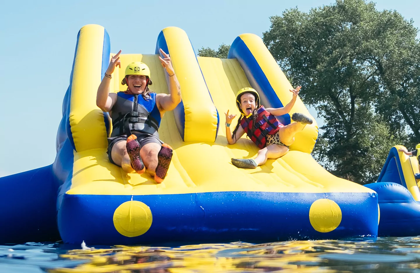 Father and daughter wearing safety helmets and life jackets sliding down an inflatable water slide at Billing Aquadrome