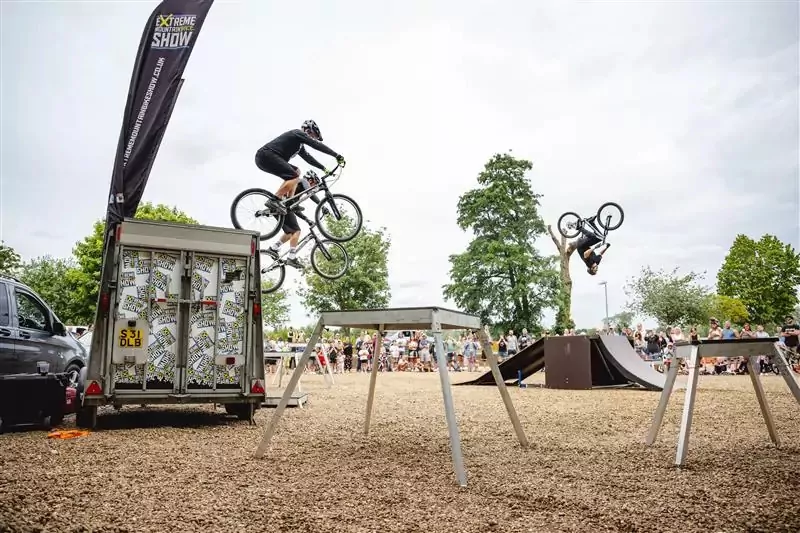 BMX and mountain bike riders performing jumps and backflips during an outdoor stunt show at Billing Aquadrome