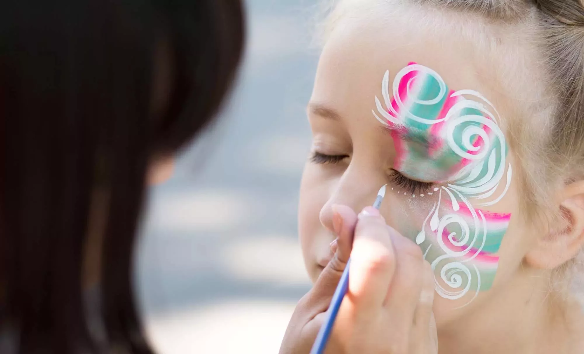 A young girl getting her face painted with colorful swirls and patterns during a fun activity at Billing Aquadrome