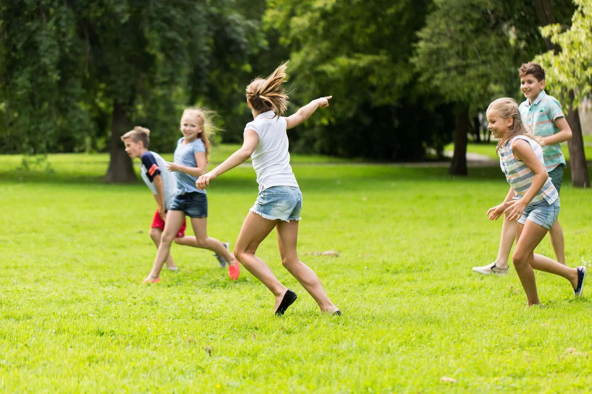 A group of children running and playing together on the grass at Billing Aquadrome during a sunny day