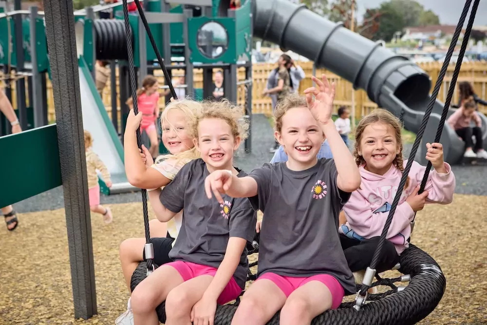 Group of smiling children playing together on a large rope swing at the playground in Billing Aquadrome