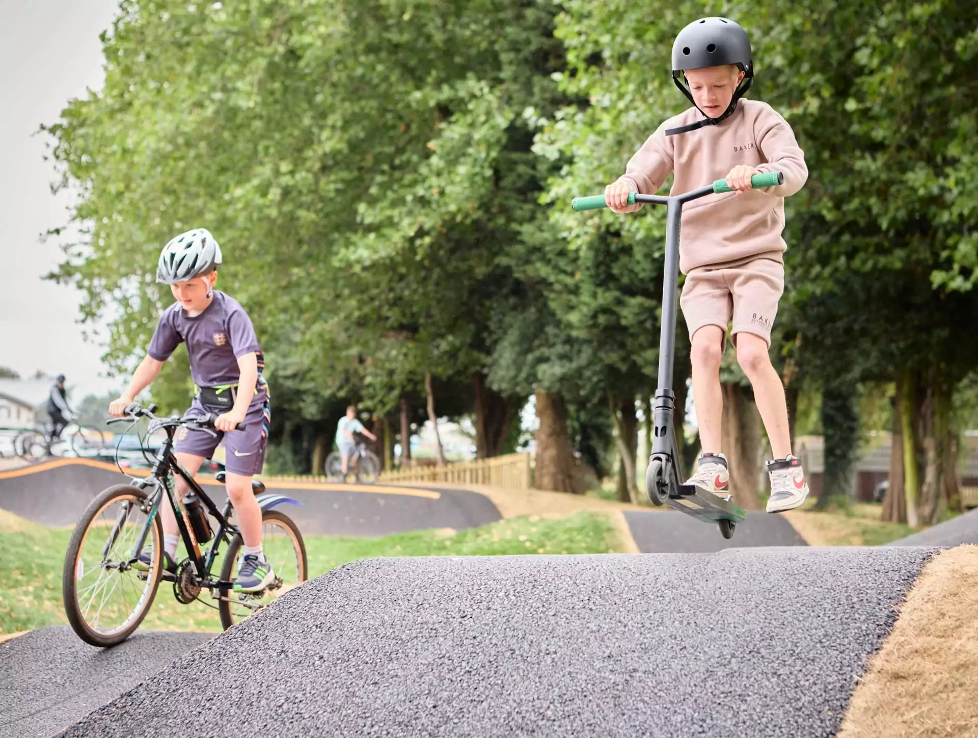 Children riding a bike and scooter on the purpose-built track at Billing Aquadrome, enjoying active outdoor fun among the trees at Meadow Bay Villages