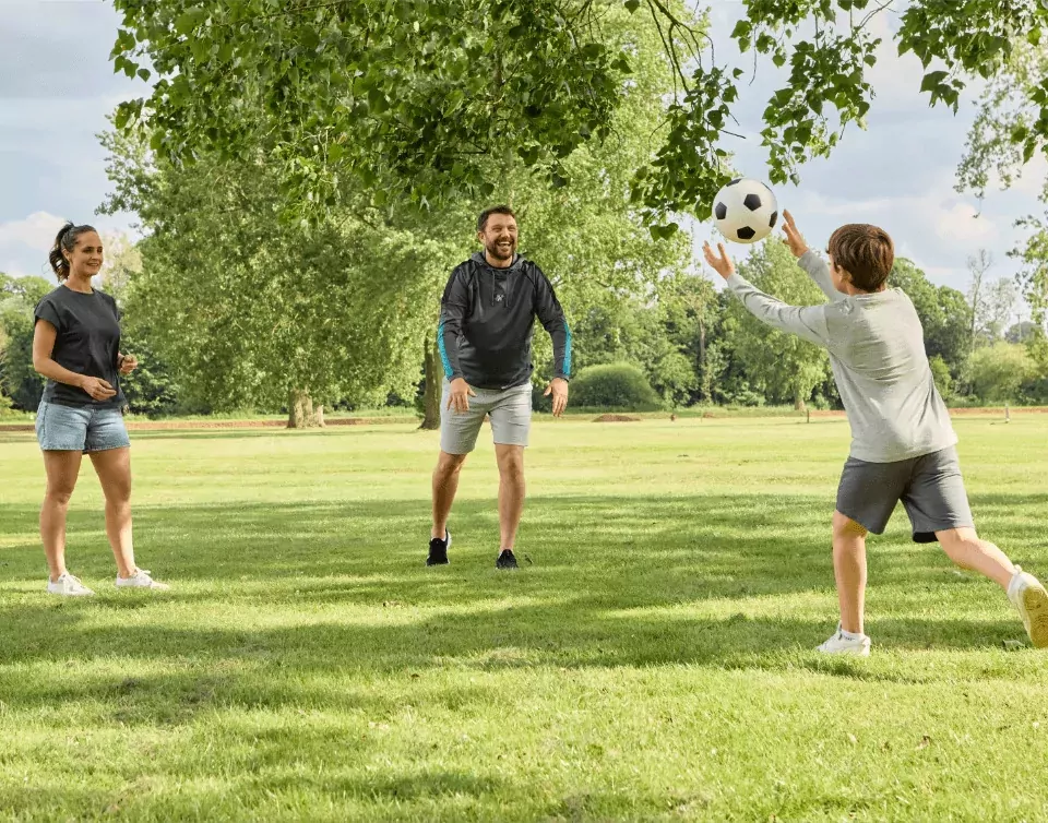 Family playing football together on a grassy field at Billing Aquadrome, enjoying active outdoor fun at Meadow Bay Villages