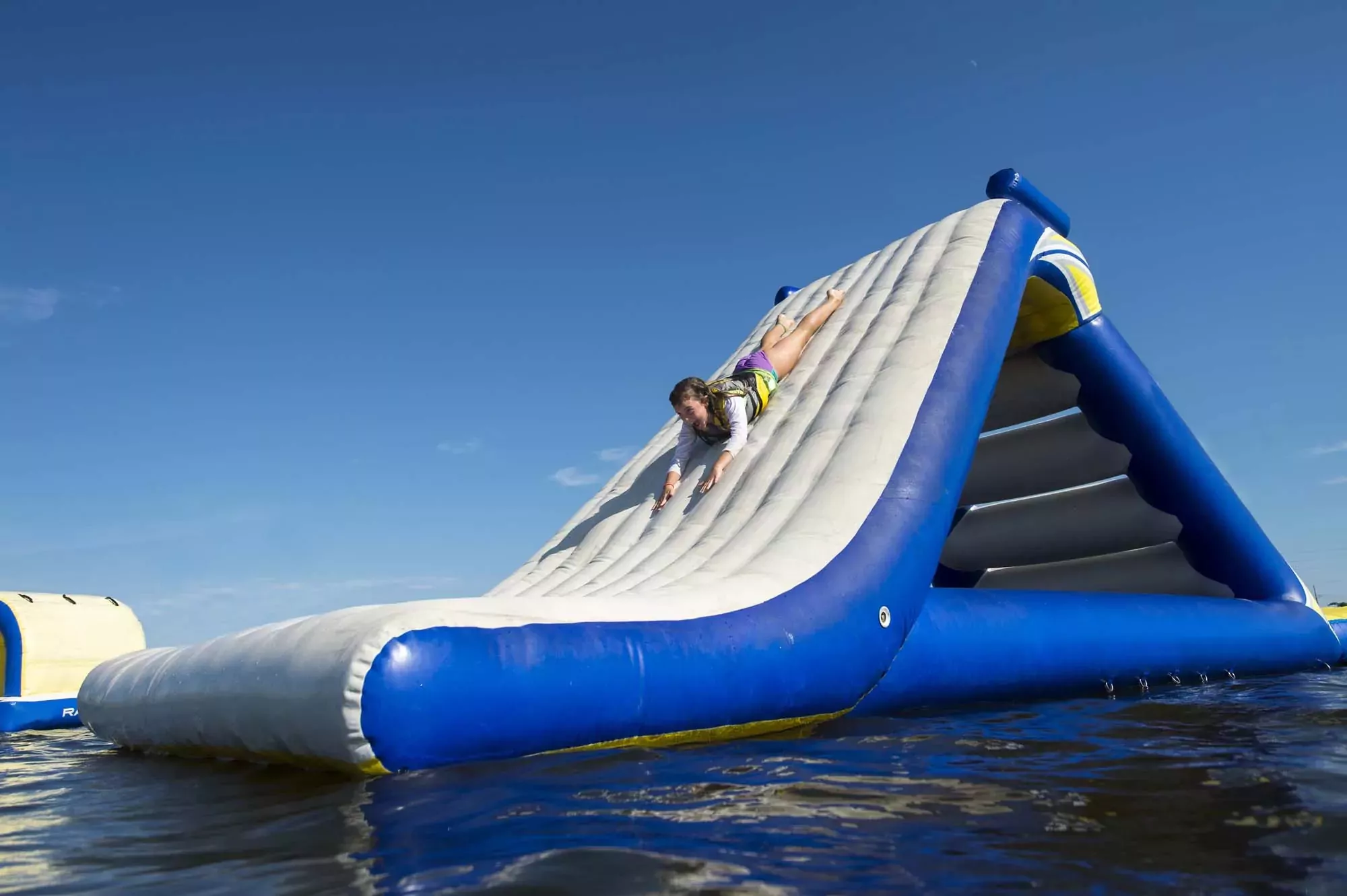 Child sliding down a giant inflatable waterslide on the lake at Billing Aquadrome holiday park, wearing a life jacket