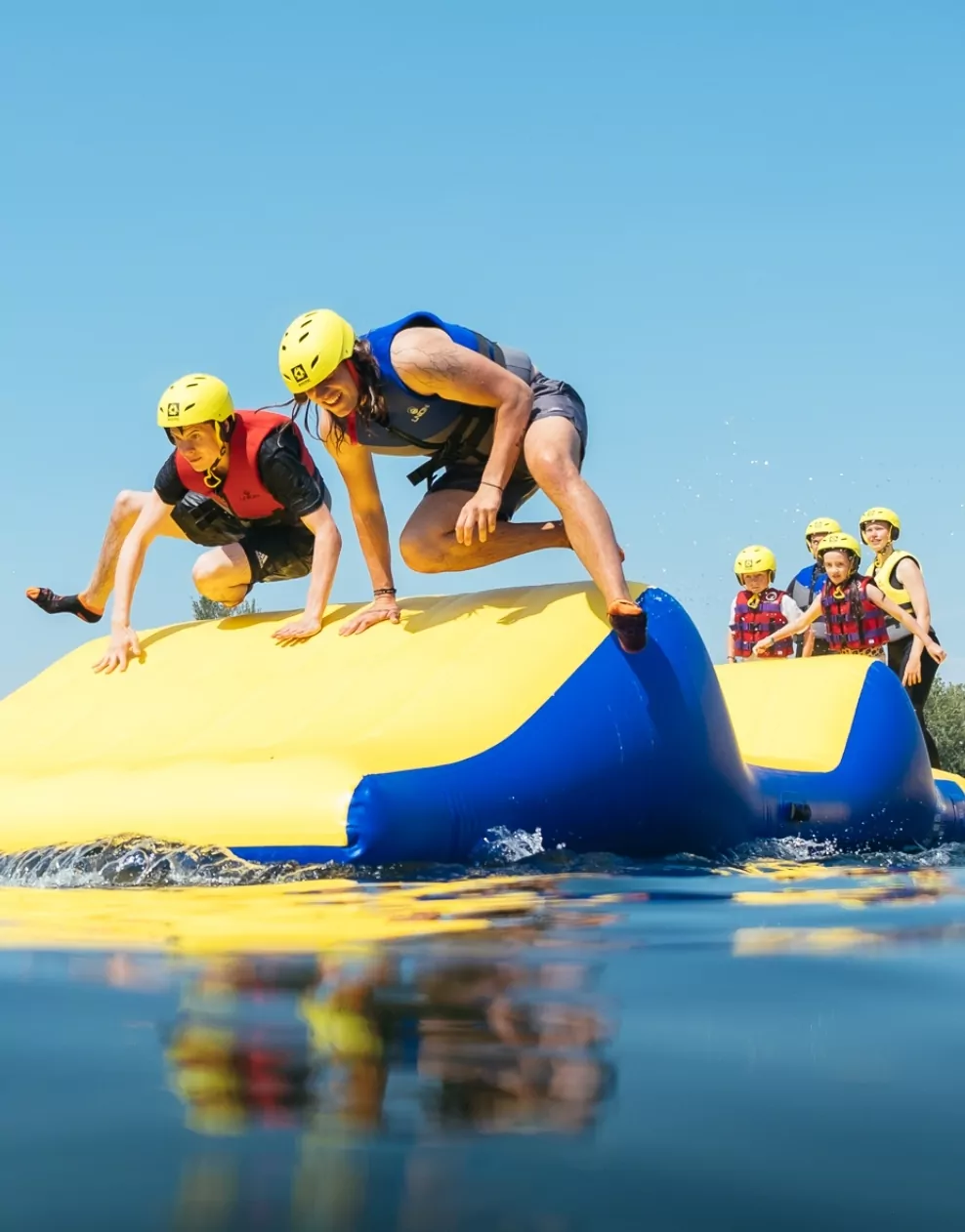 People wearing helmets and life jackets climbing on a large inflatable at the water park in Billing Aquadrome