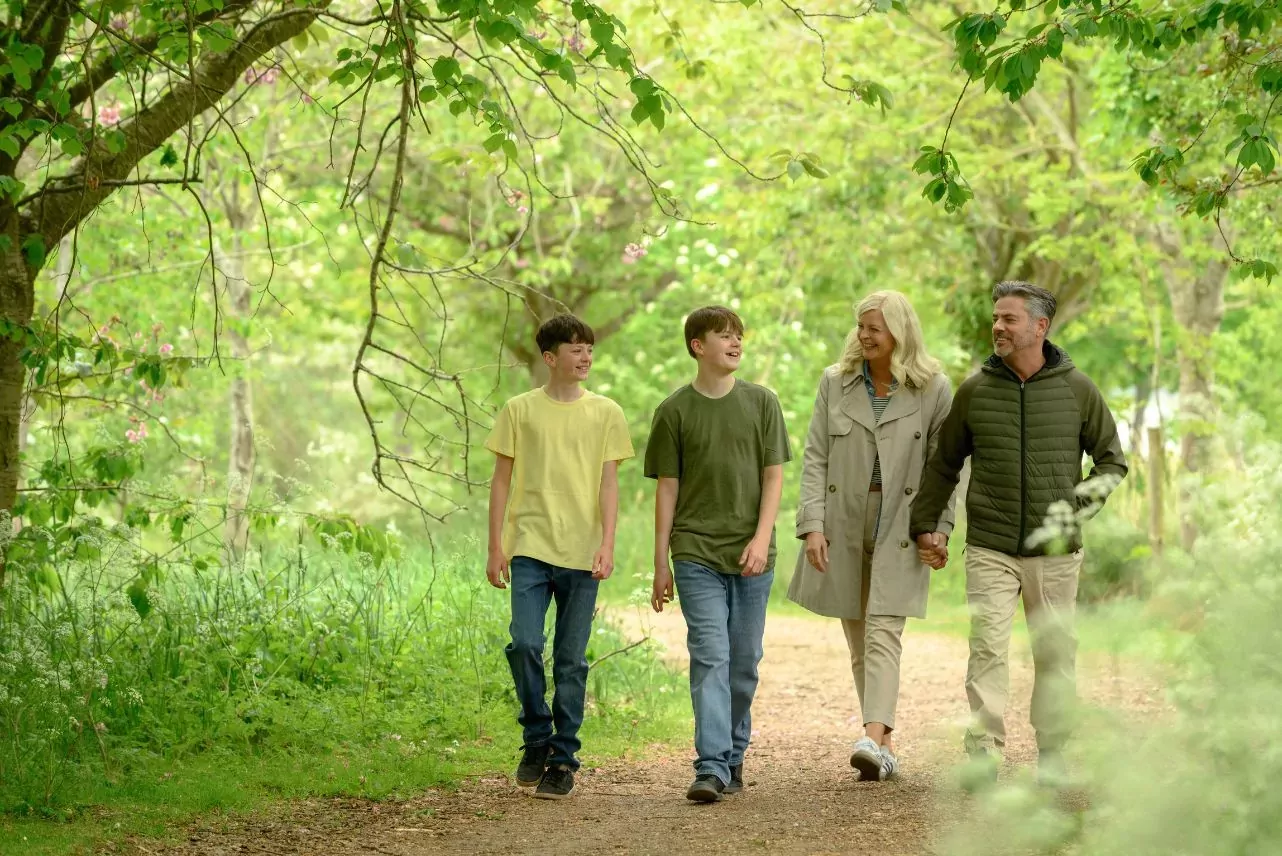 Family enjoying a woodland walk along a scenic nature trail at Billing Aquadrome, surrounded by trees and greenery at Meadow Bay Villages
