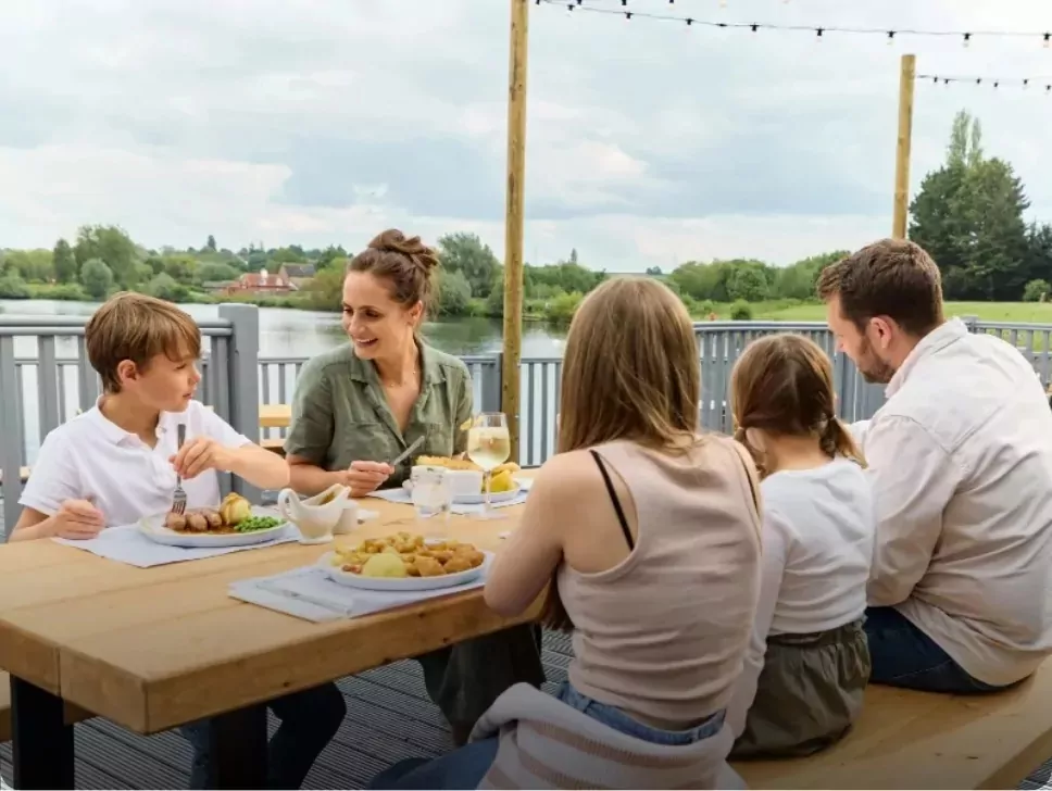 Family enjoying al fresco dining on a decked terrace overlooking the water at Meadow Bay Villages’ Billing Aquadrome