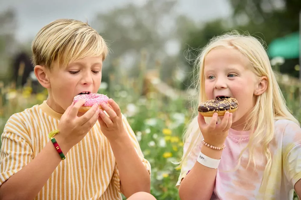 Two young children enjoying colourful donuts in a field of wildflowers at Billing Aquadrome holiday park