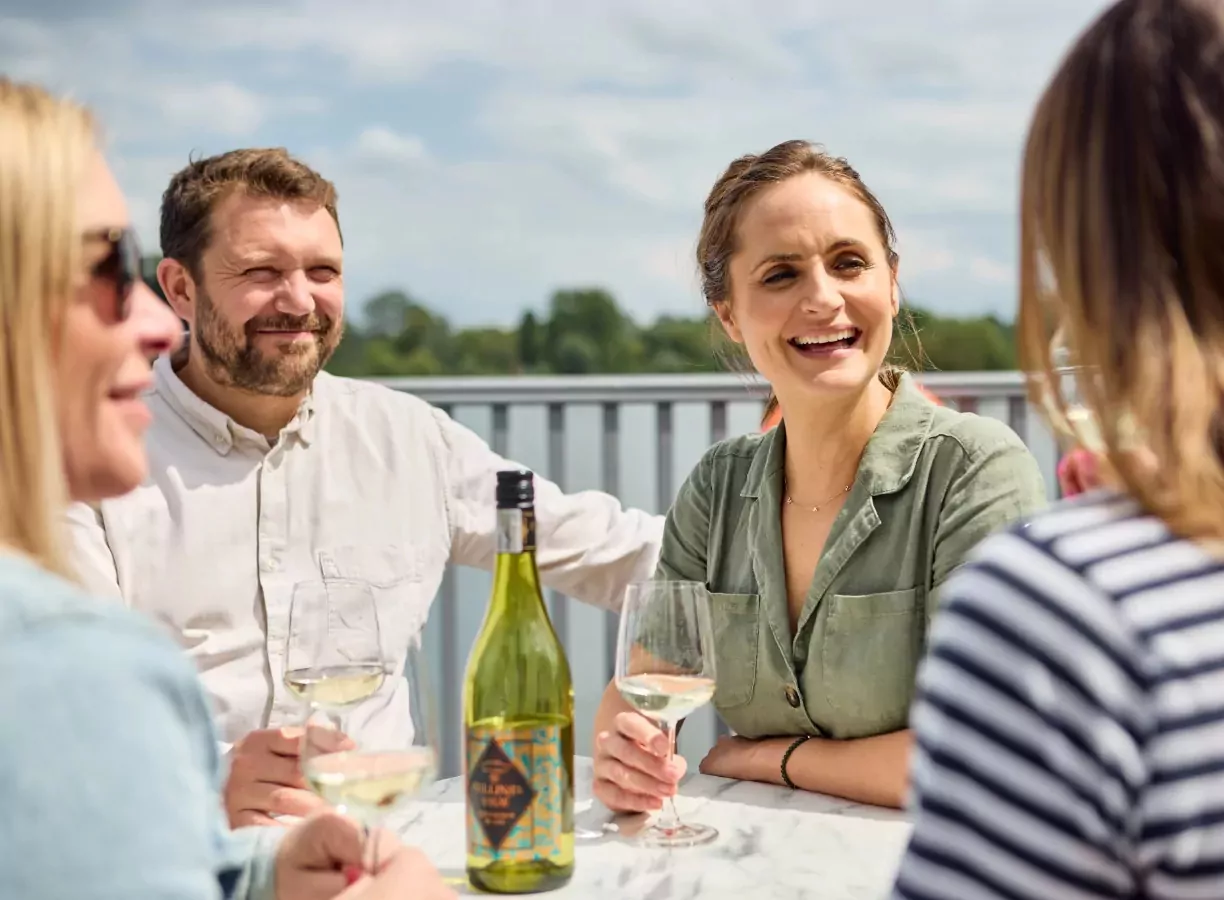 Group of adults enjoying white wine and conversation at an outdoor table overlooking the water at Billing Aquadrome holiday park
