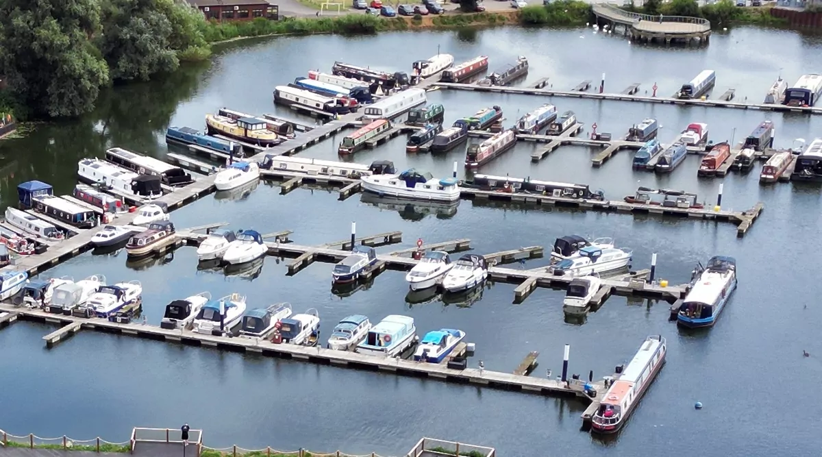 Aerial view of the marina at Meadow Bay Villages’ Billing Aquadrome, showing a variety of boats and narrowboats moored on calm water surrounded by greenery