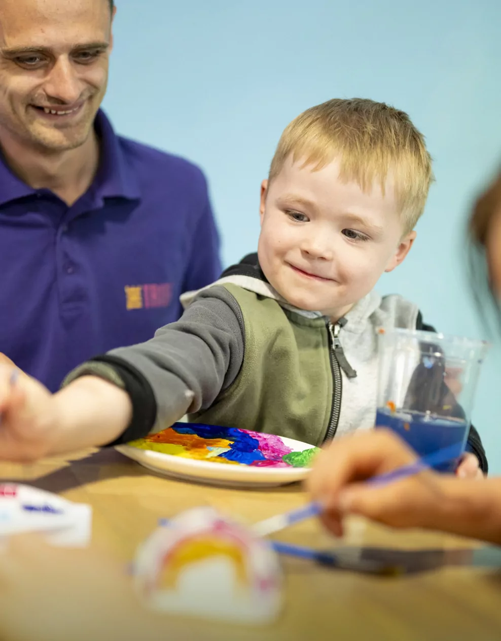 A young boy smiling while painting pottery with bright colours during a craft activity at Billing Aquadrome.