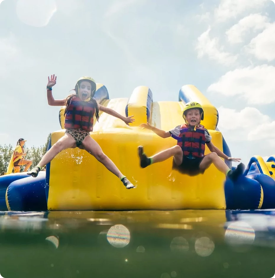 Children jumping into the water from the inflatable aqua park assault course at Billing Aquadrome.