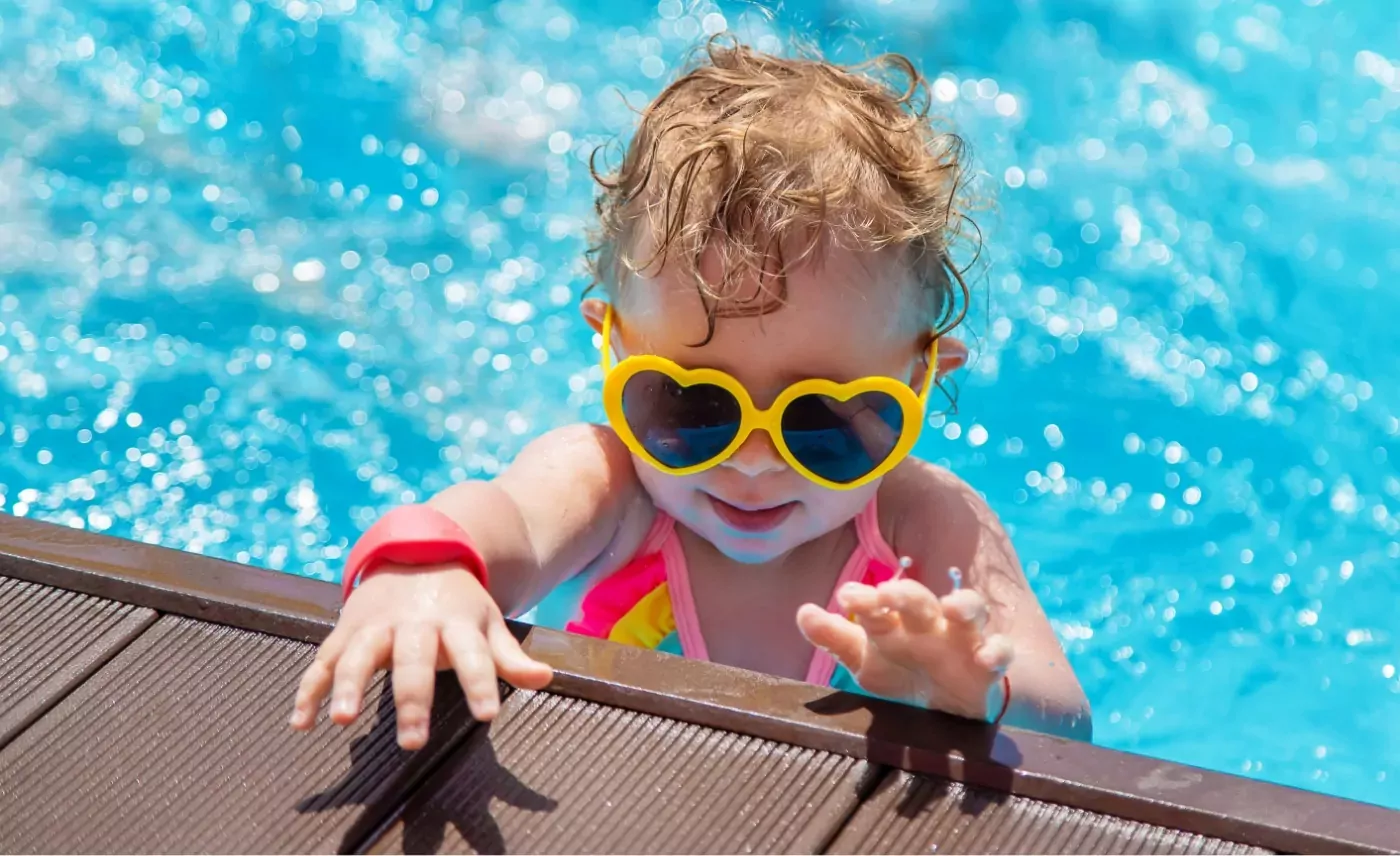 Toddler in heart-shaped sunglasses enjoying a sunny swim at the children’s pool in Meadow Bay Villages' Golden Leas holiday park.