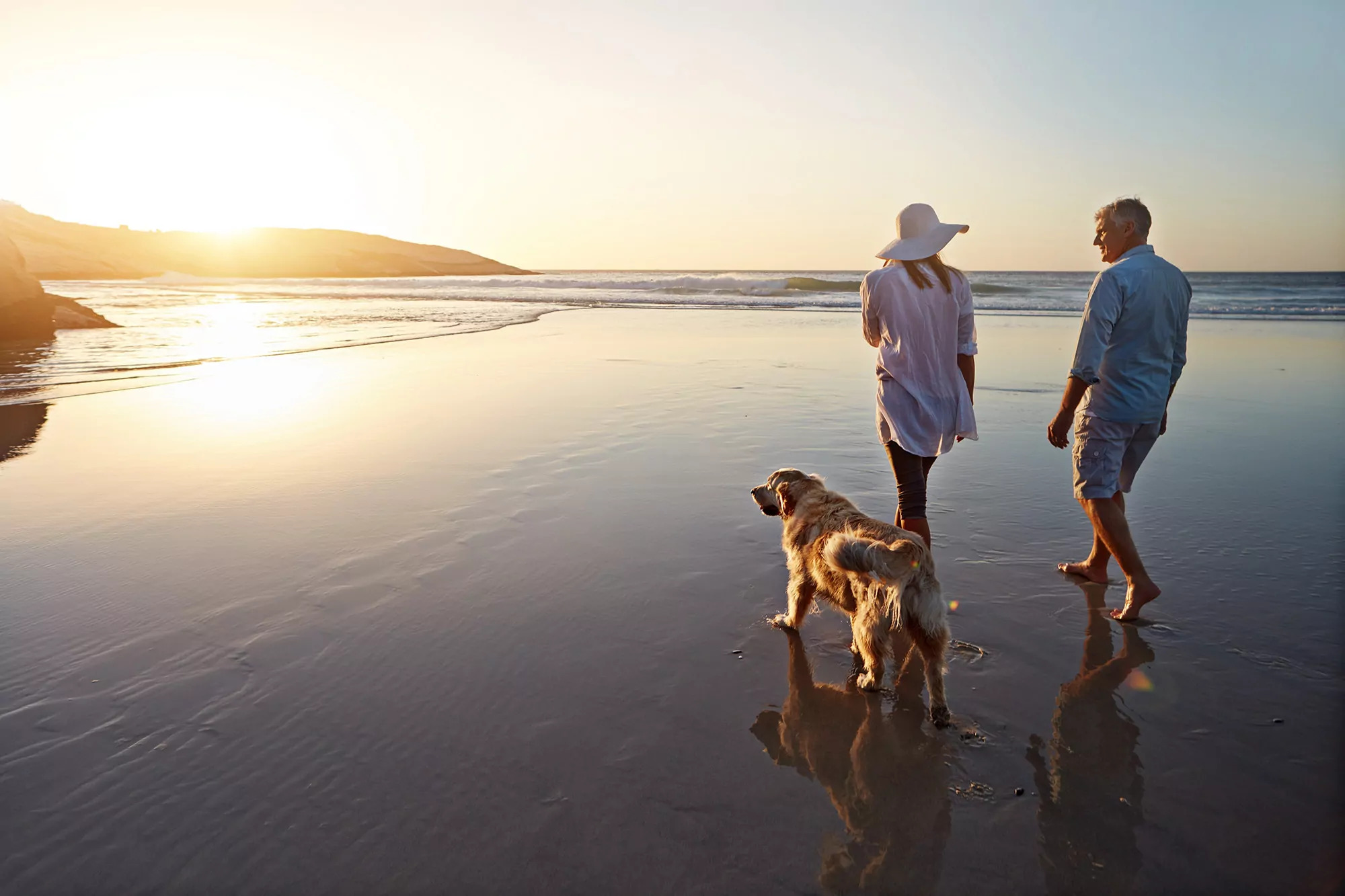 Couple walking their dog along the beach at sunset near Meadow Bay Villages' Golden Leas, enjoying a peaceful and pet-friendly seaside escape.