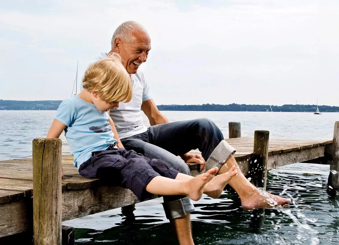 Grandfather and grandson sitting on a wooden pier, dipping their feet in the water and enjoying the seaside at Golden Leas.