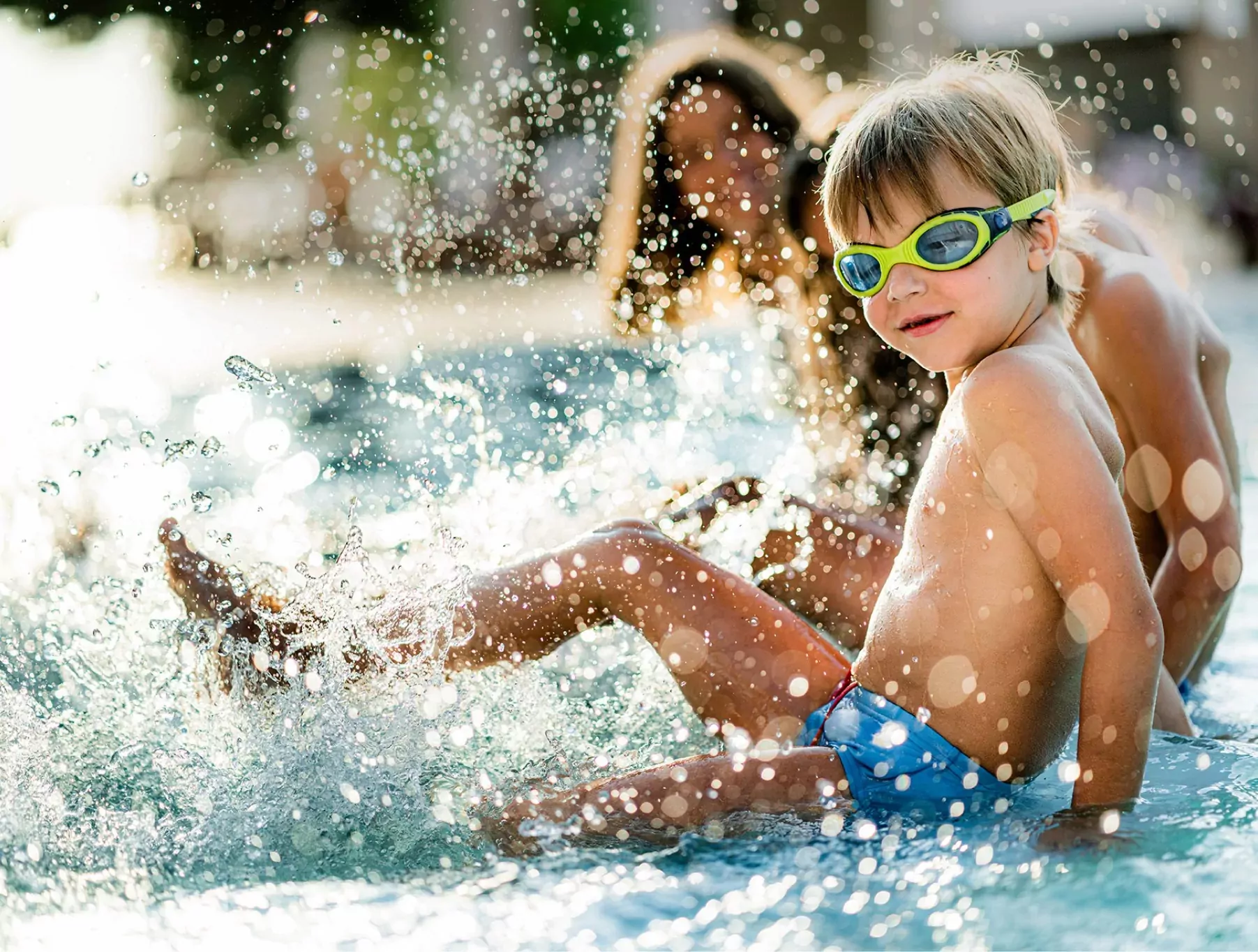 Young boy splashing in an outdoor pool with goggles on, enjoying summer fun at Golden Leas.
