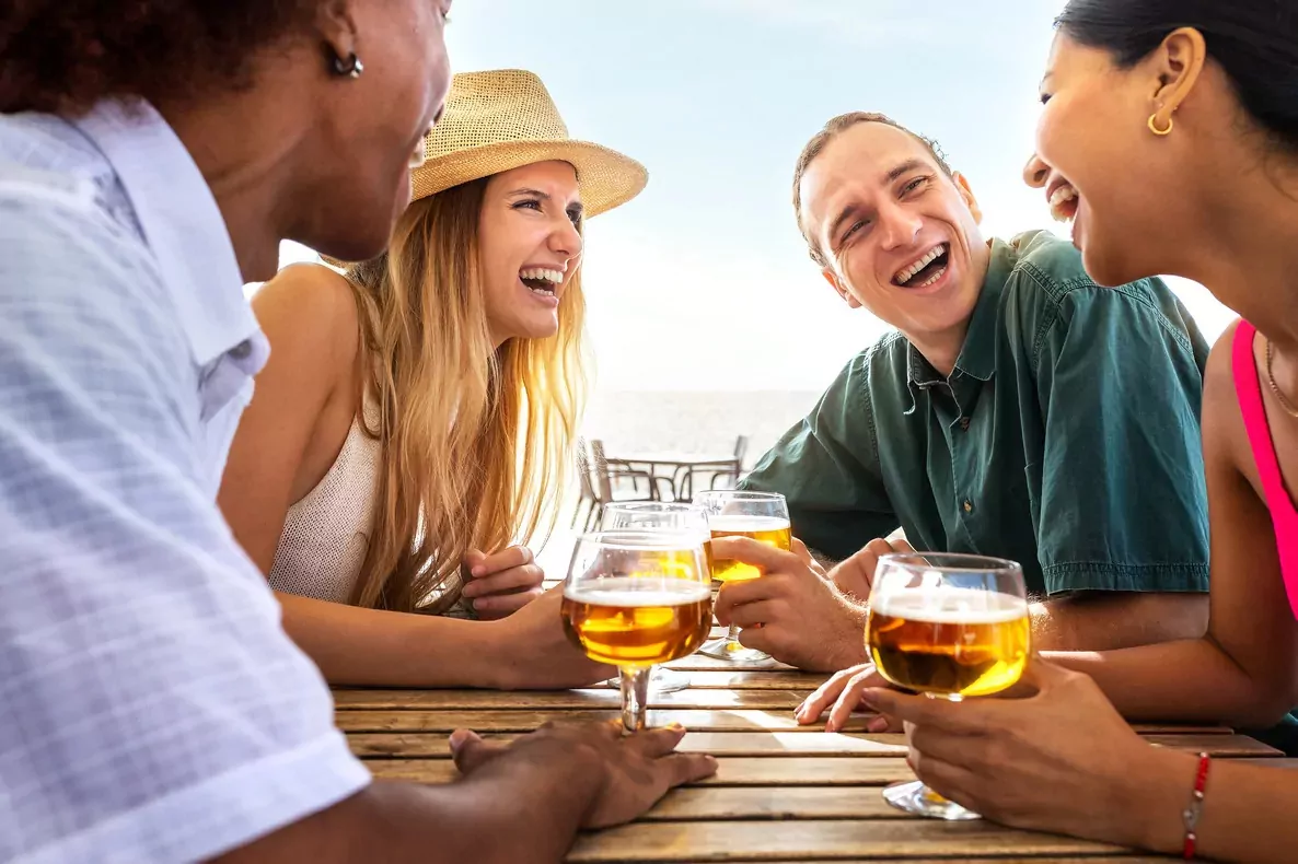Group of friends laughing and enjoying drinks by the seaside near Golden Leas.