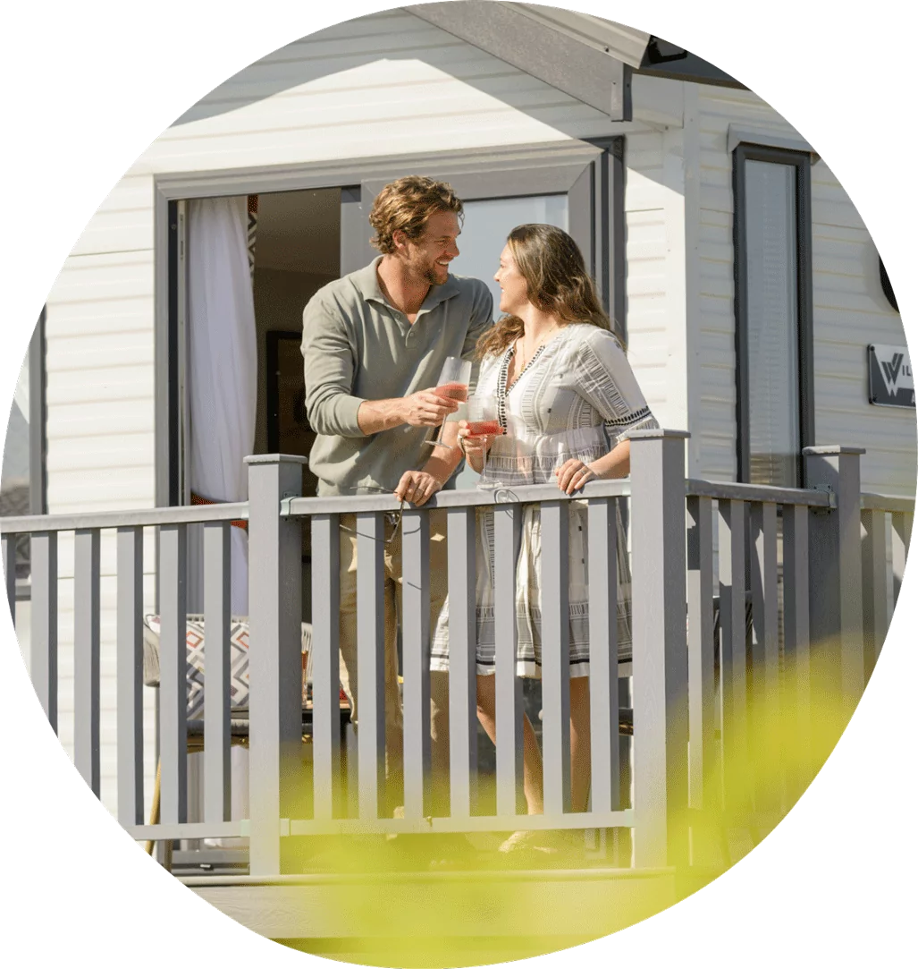 Couple relaxing on the decking of a holiday caravan holding drinks and enjoying their stay at Golden Leas