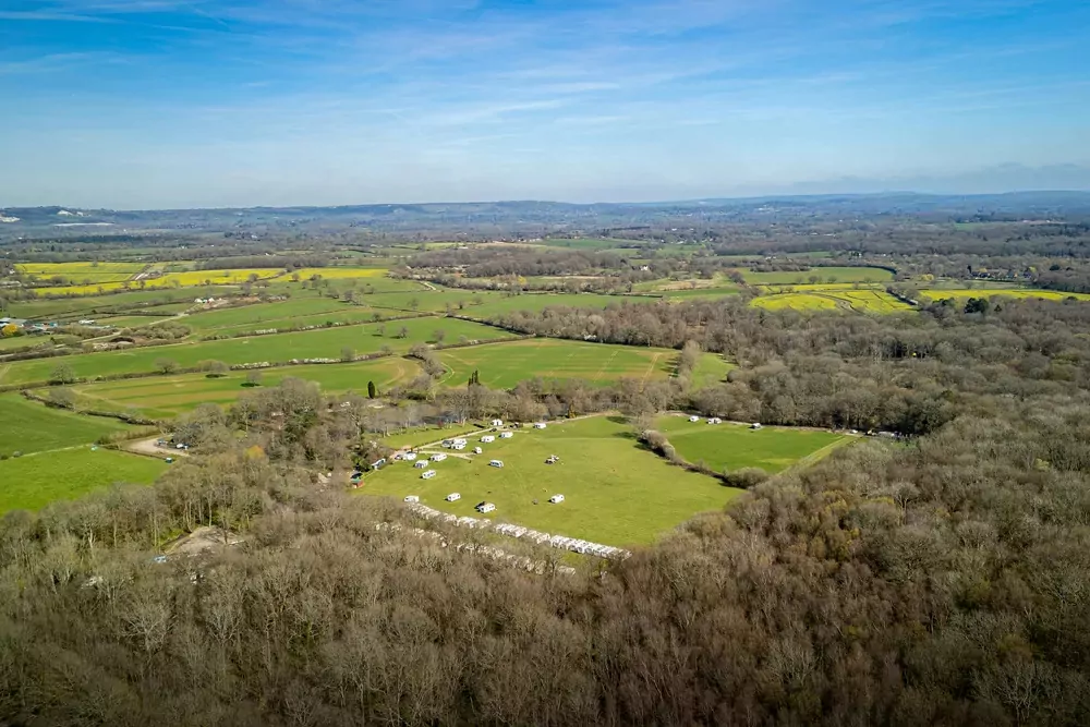 High-angle aerial view of the lush green countryside and camping fields at Henfold Lakes.