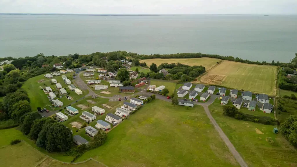 Aerial view showing caravans, holiday homes, green fields, and coastal sea views at Hollybush Farm
