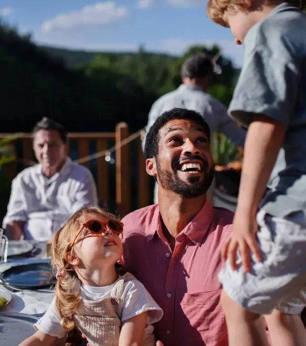 Smiling father on Hayling Island looking up joyfully at his son while holding his young daughter wearing sunglasses, enjoying outdoor family time together.