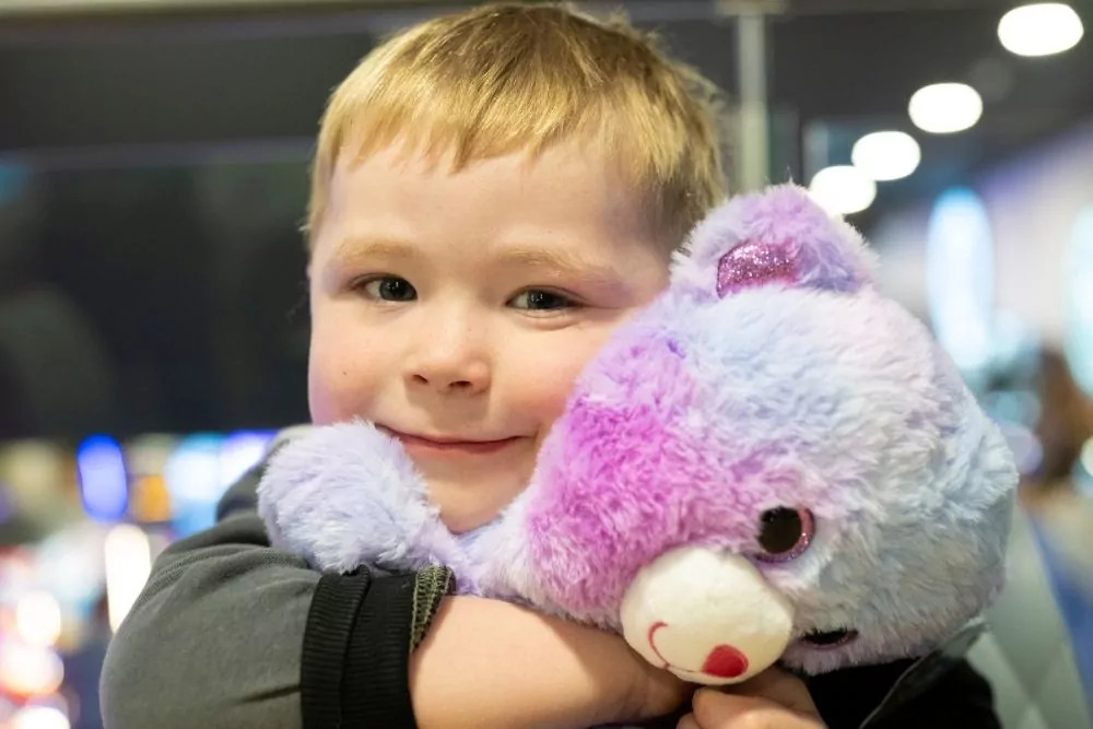 Smiling young boy hugging a soft purple and pink teddy bear at Hayling Island.