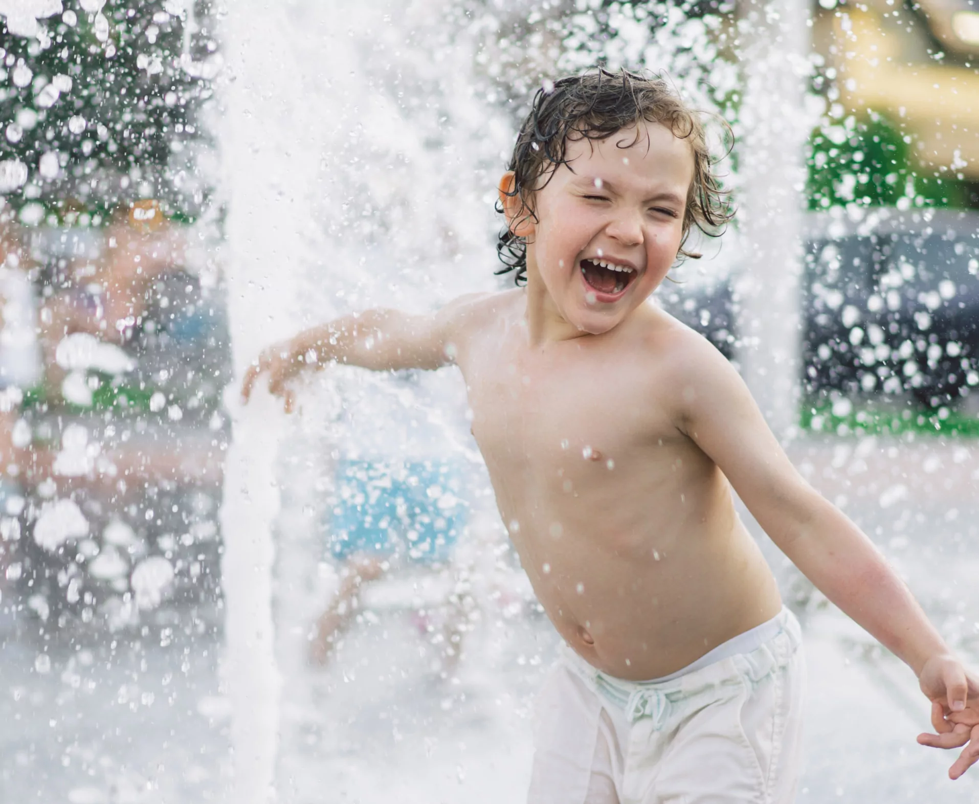 A young boy joyfully splashes in a water park, surrounded by sparkling droplets and sunlight.