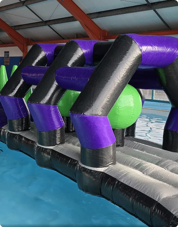 A large inflatable obstacle course in a swimming pool, featuring black, purple, and green structures designed for an exciting and challenging water adventure.