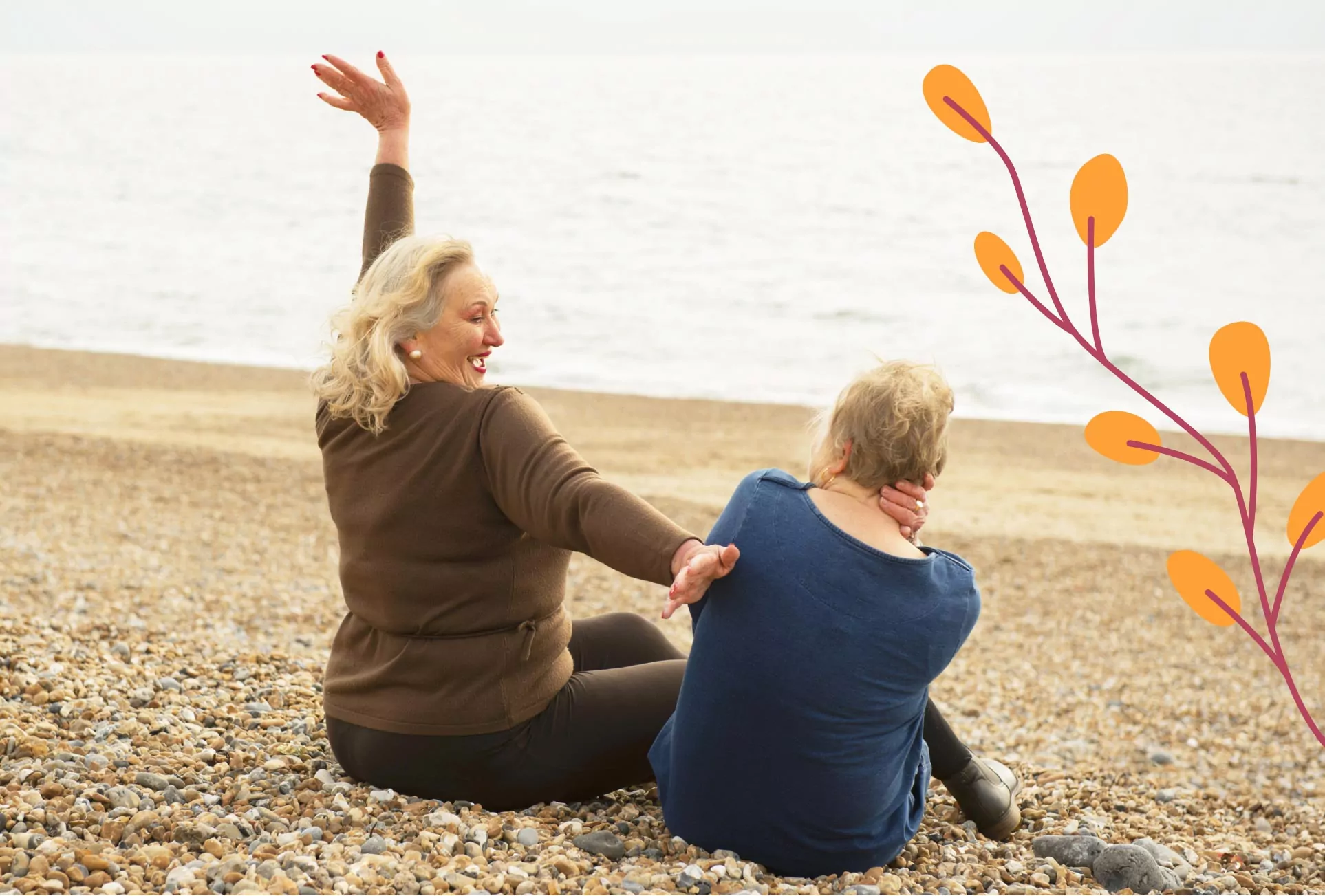 Two older women sitting on a pebble beach by the sea, enjoying a relaxed and cheerful moment. One woman raises her arm in excitement while the other looks out at the ocean.