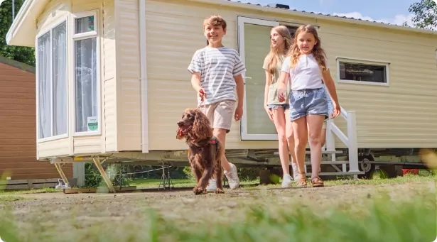 A group of children walking a dog outside a caravan