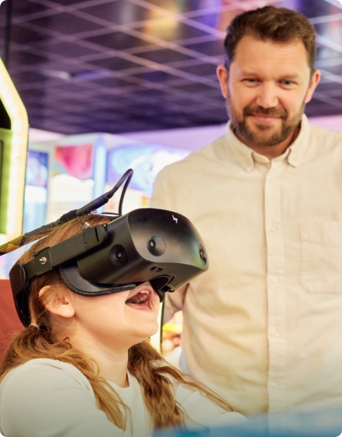Young girl playing on a VR headset whilst their dad watches on