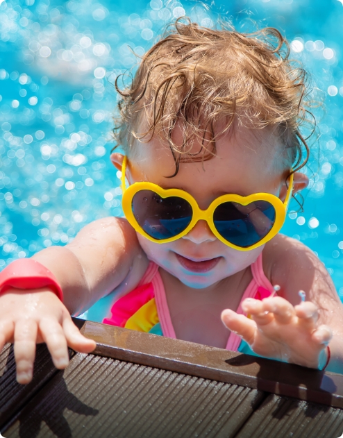 A young girl wearing yellow heart shaped sunglasses, sat in a pool