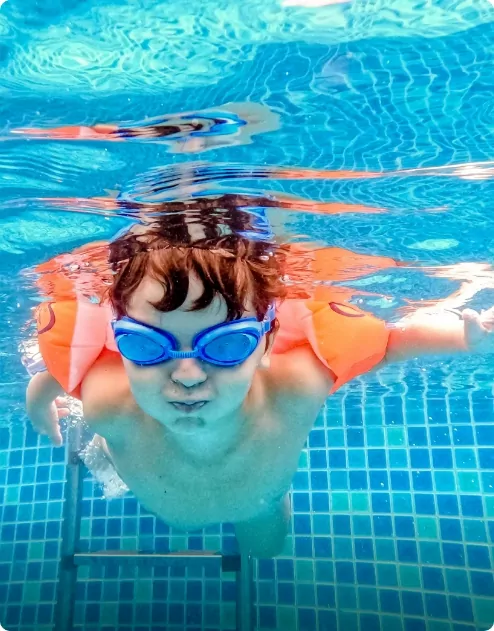 A young child with arm bands and goggles on swimming underwater in a pool