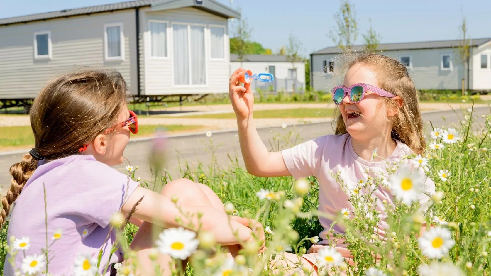 Two young girls laughing and playing with bubbles in a wildflower meadow near holiday caravans on Hayling Island.