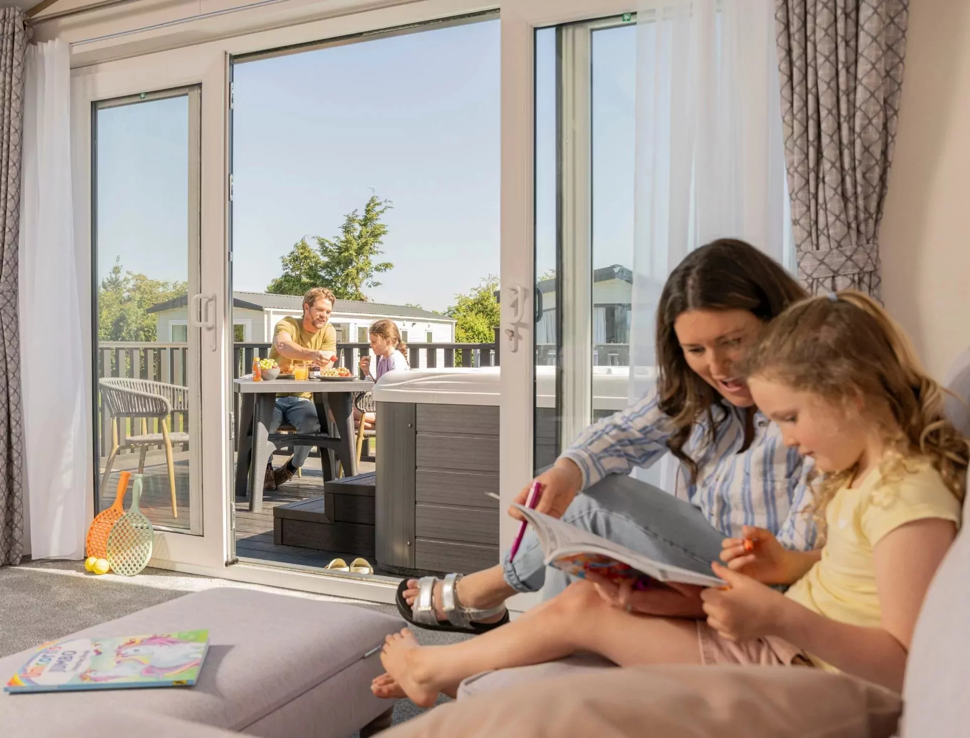 A family enjoying quality time together inside their holiday caravan while others dine outside on the decking on Hayling Island.