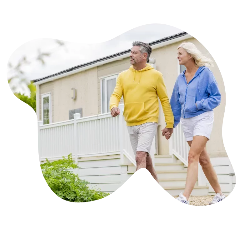 A middle-aged couple holding hands and walking past a holiday home, the man in a yellow hoodie and white shorts, and the woman in a blue hoodie and white shorts, Hayling Island.