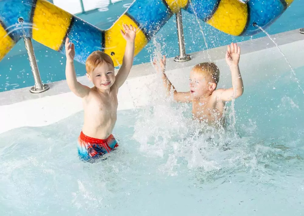 Two happy young boys playing joyfully in a vibrant indoor splash park with water spraying around them Hayling Island