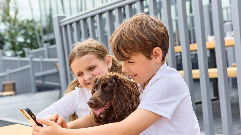 Two smiling children taking a selfie with their brown dog while sitting at an outdoor table in Hayling Island.