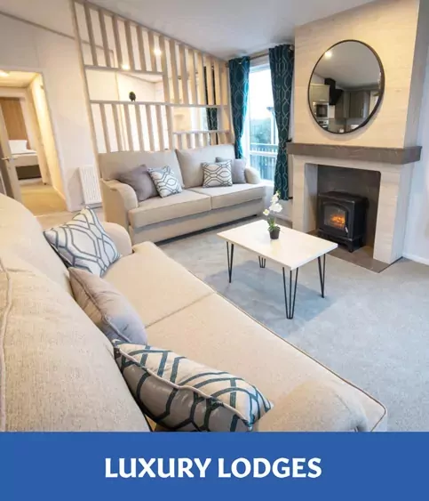 An elegant "Luxury Lodge" interior featuring two cream sofas with decorative pillows, a coffee table, a fireplace with a wood-burning stove, and dark teal curtains, Hayling Island.