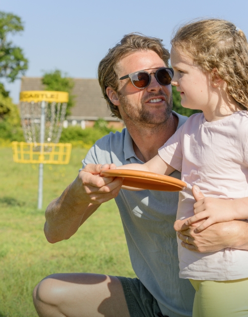 Father teaching his young daughter how to play disc golf together on a sunny day at Hayling Island