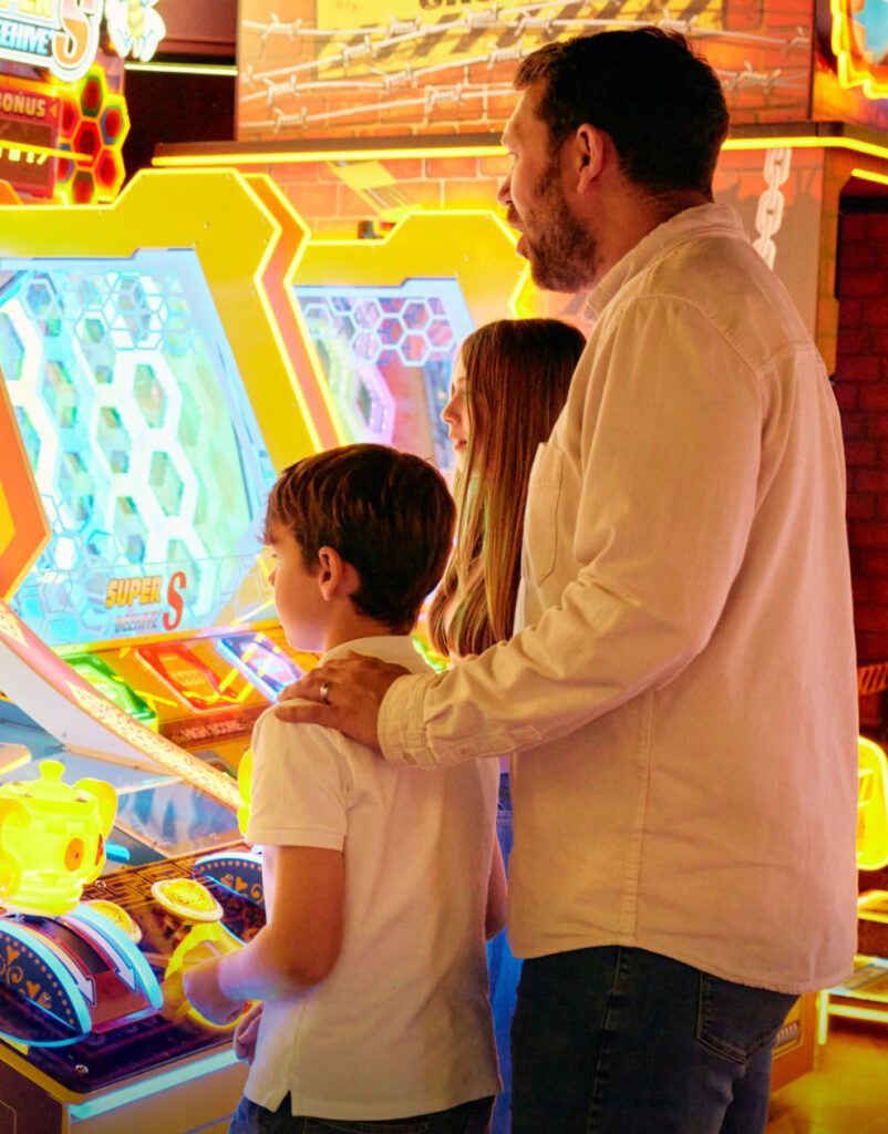 A father and his two children play on a bright, neon-lit arcade game inside the entertainment complex at Hayling Island.