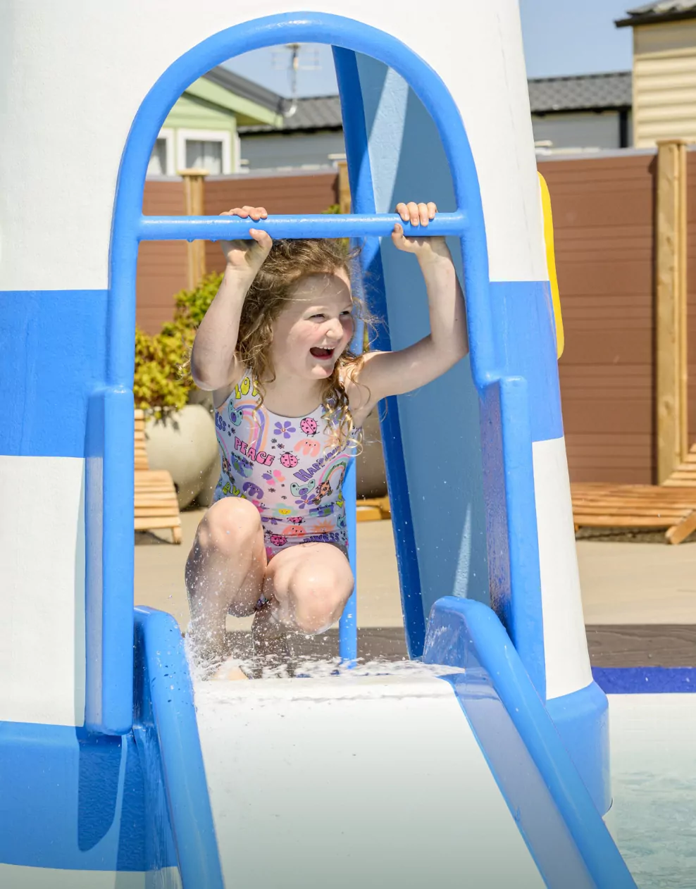 A young girl smiles while sliding down the lighthouse feature at the outdoor splash park at Hayling Island.