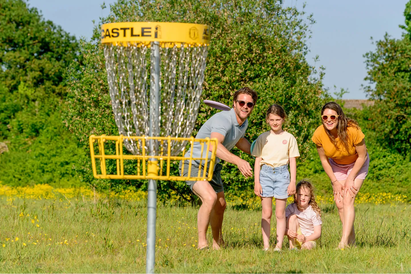Family playing disc golf together on a sunny grassy activity field during a holiday park activity on Hayling Island.
