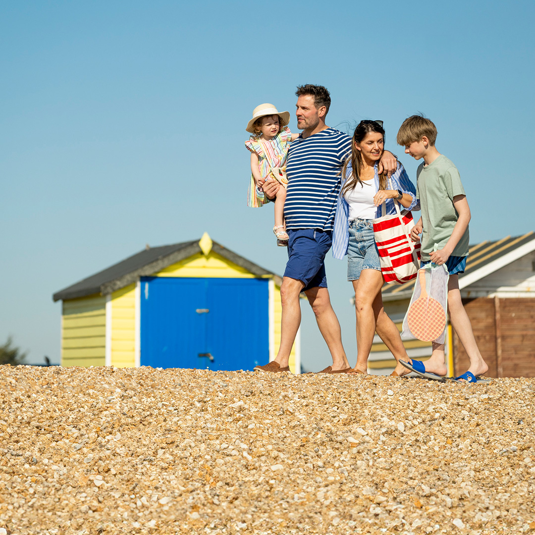 Family walking together along the pebble beach past colorful beach huts near Meadow Bay Villages Hayling Island