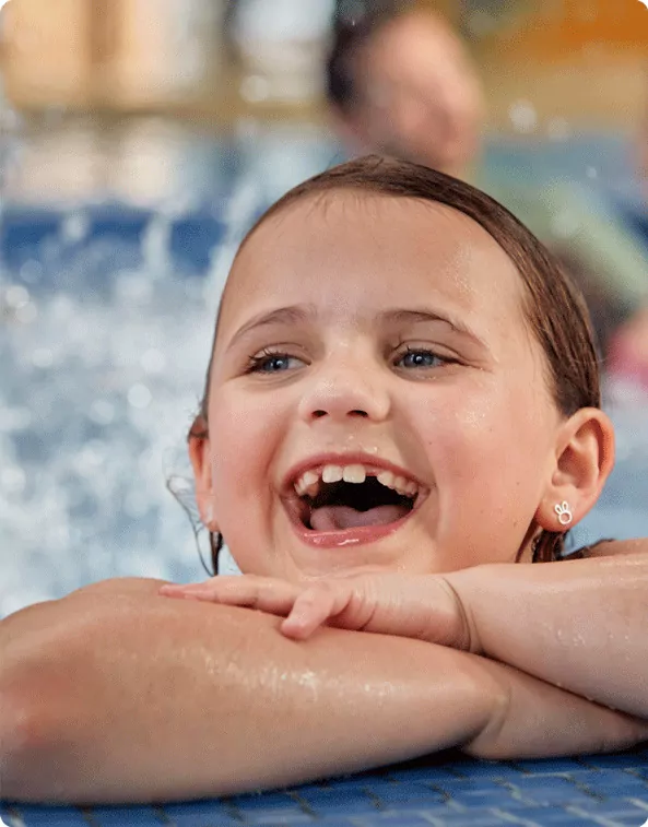Smiling young girl resting on the edge of a swimming pool, enjoying a fun day in the water at Hayling Island.