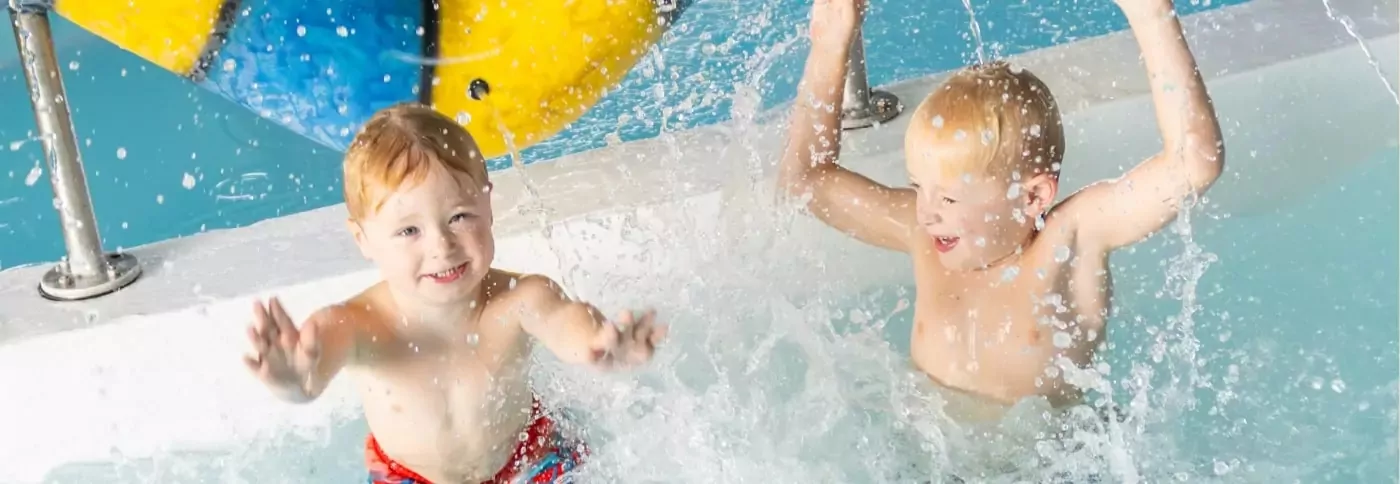 Two young boys laughing and splashing playfully in a bright blue swimming pool, Hayling Island.