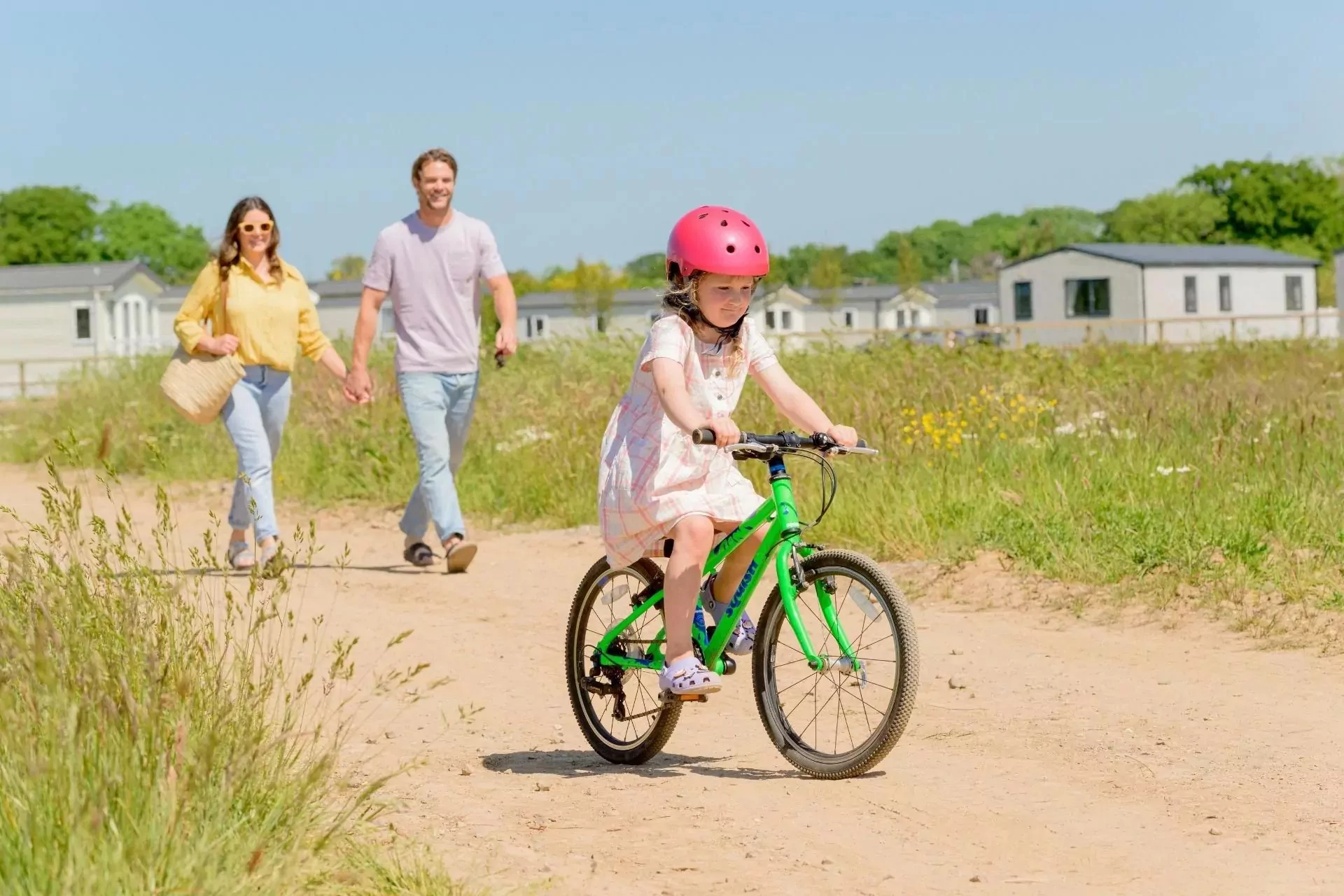 A young girl riding her bike along a sunny trail with her parents walking behind her on Hayling Island.