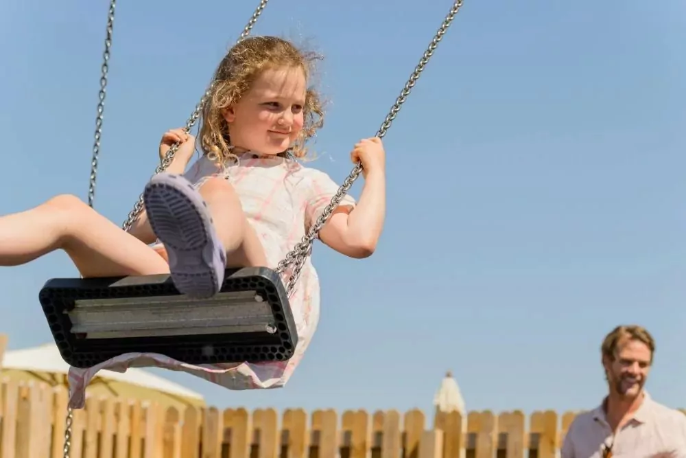 A smiling girl enjoying the swings in the outdoor playground on Hayling Island.