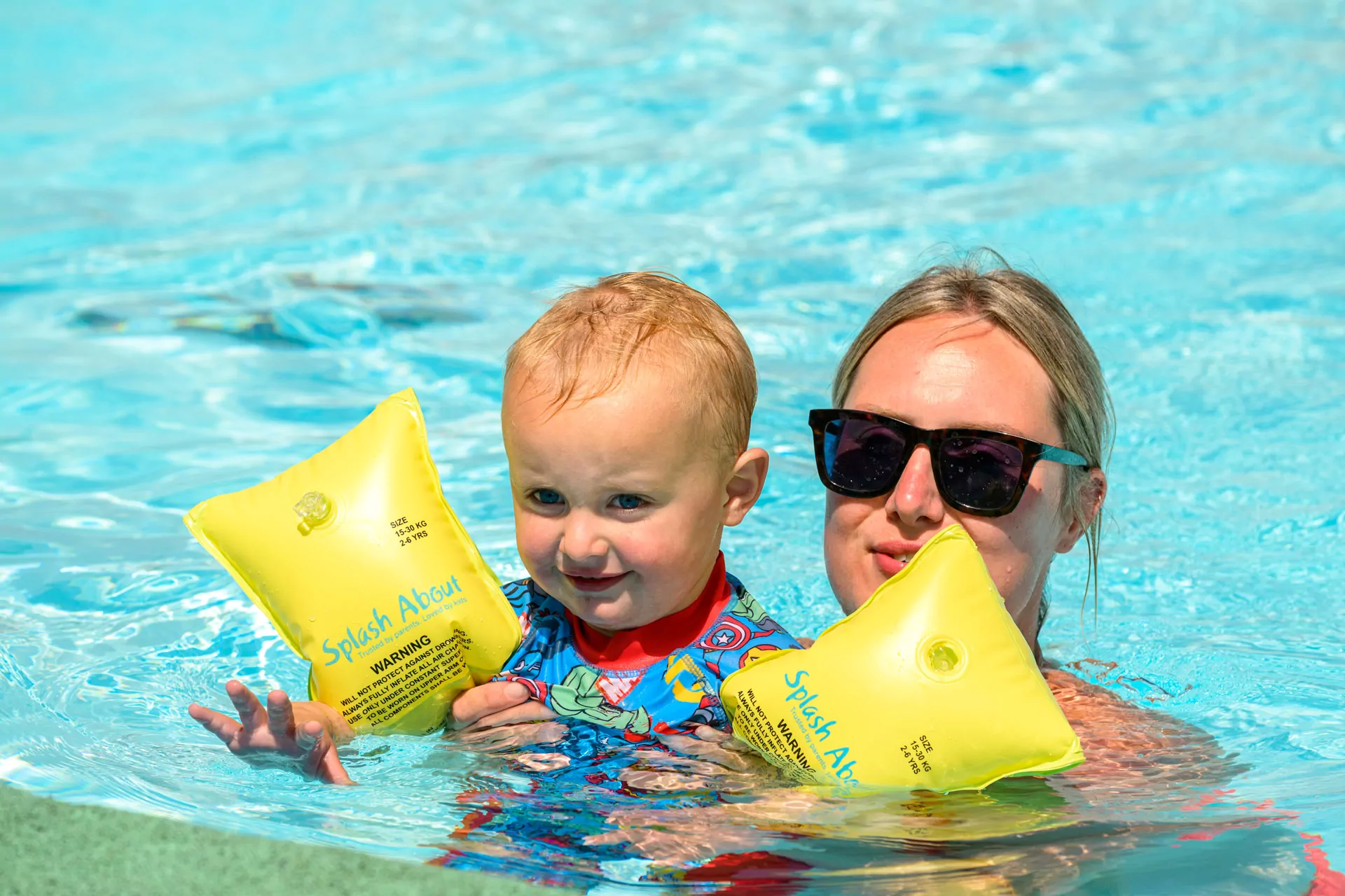 A toddler wearing bright armbands enjoying a safe and sunny swim with a parent on Hayling Island.